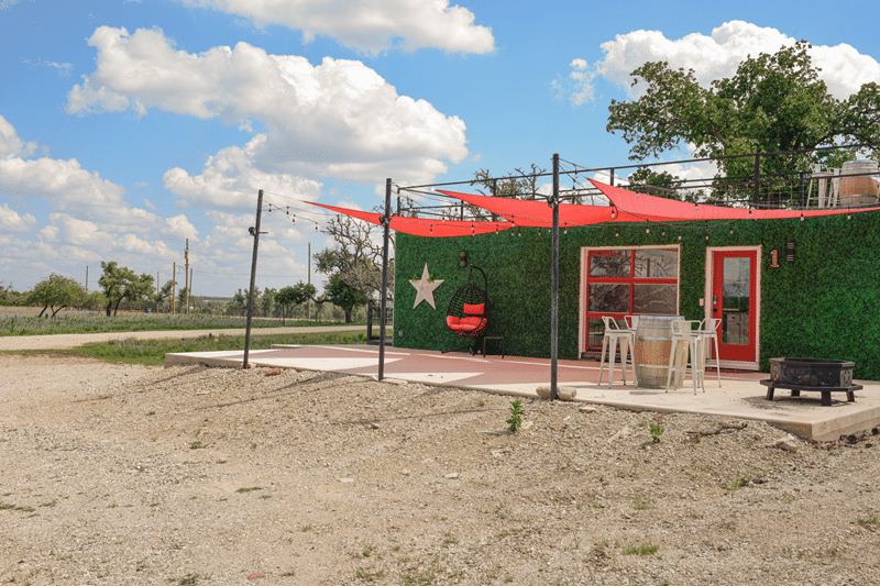 Romantic outdoor seating area at Fredericksburg Bed and Breakfast with a star-adorned wall, red canopies, and a hanging chair, set against a scenic Texas landscape.